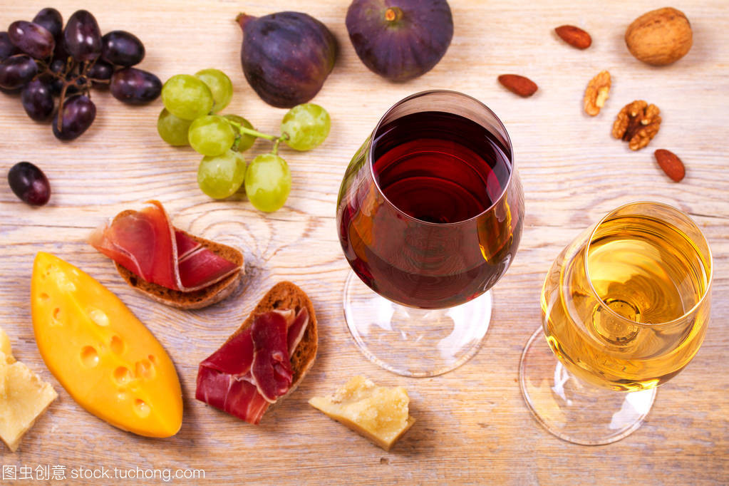 紅色和白色奶酪、 火腿、 無花果和葡萄與葡萄酒杯。木制的桌子上的酒杯。葡萄酒的靜物